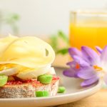 A delicious breakfast setup with cheese, eggs, and orange juice, accompanied by a purple flower.