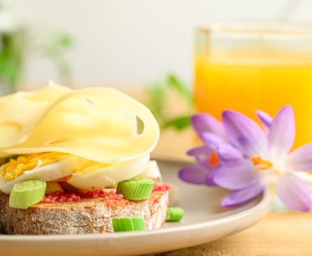 A delicious breakfast setup with cheese, eggs, and orange juice, accompanied by a purple flower.