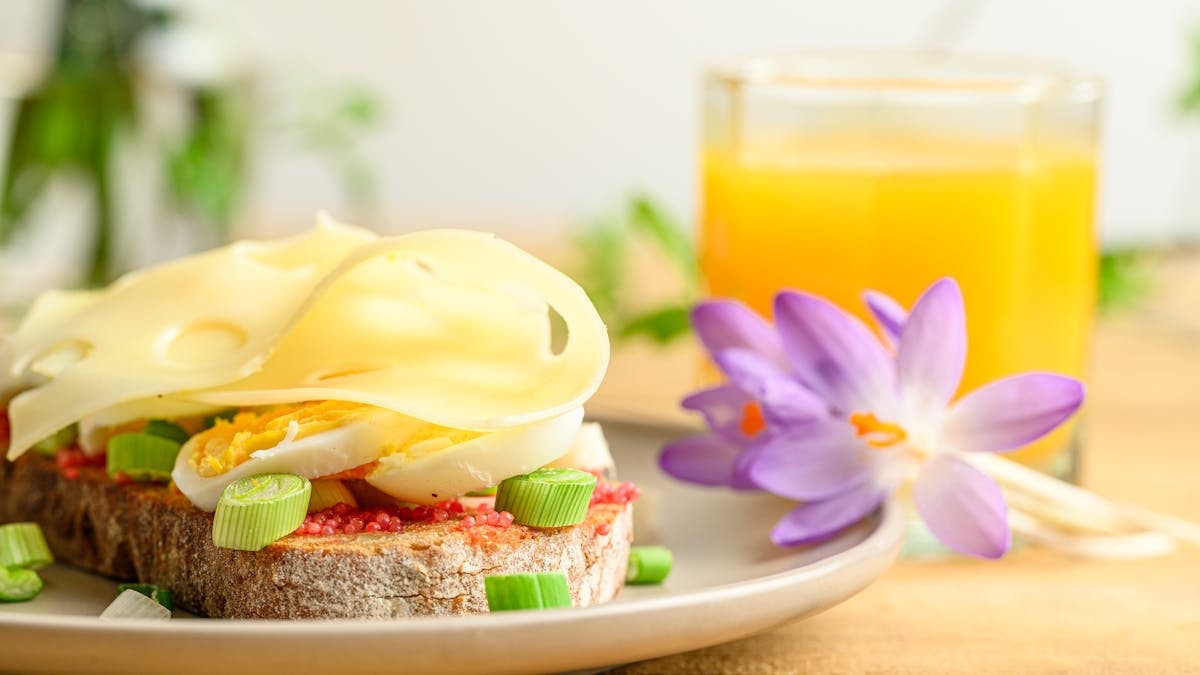 A delicious breakfast setup with cheese, eggs, and orange juice, accompanied by a purple flower.