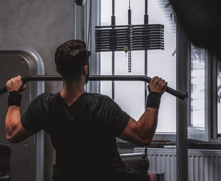 Back view of a man exercising with lat pulldown machine in the gym.